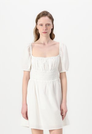 Rochie albă cu decolteu pătrat, mâneci bufante și bust elastic. Material moale, neted, cu un aspect ușor și aerisit.
