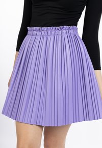 Fustă plisată violetă, realizată dintr-un material ușor, cu un talie cu volane și o textură netedă, având pliseuri verticale distanțate uniform.