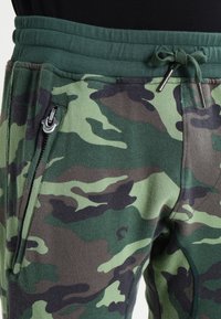 Gröna kamouflagejoggers med dragsko i midjan, mjuk textur och detaljer med zip-fickor på sidan.