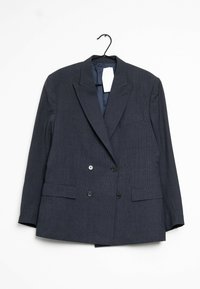 Blazer double boutonnage gris foncé avec un tissu texturé, deux poches avant et des boutons noirs. Accroché à un crochet noir. Étiquette visible à l'intérieur.