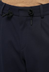 Παντελόνι σε σκούρο μπλε με υφή, με ελαστική μέση, μαύρα κορδόνια και πλαϊνές τσέπες. Ο σχεδιασμός τονίζει την άνεση και τη σωστή εφαρμογή.