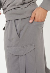 Grå bomullsjoggers med ribbad midja, sidficka och ett vikt klafffickdetalj, avslutade med en subtil logotyp i grönt.