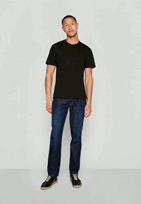 Black short-sleeve T-shirt with a classic crew neck, paired with dark blue denim jeans and black sneakers with a light sole.