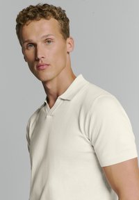 Korte mouwen polo shirt van crèmekleurige gebreide stof. Bevat een kraag, een lichte V-hals en ribgebreide boorden, met een gladde, gelijkmatige textuur.