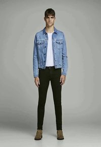 Casaco de ganga azul claro com dois bolsos no peito, t-shirt branca, jeans skinny pretos e botins castanhos de cano curto. Design simples, forma ajustada.