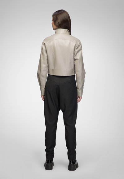 Giacca in pelle grigia chiara, tagliata, con colletto alto, abbinata a pantaloni neri a sigaretta e scarpe nere massicce. Texture liscia, design minimalista.
