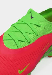 Πράσινο και κόκκινο ποδοσφαιρικό παπούτσι Nike με πράσινα κορδόνια και ορατές προεξοχές στη σόλα, σχεδιασμένο για απόδοση στο γήπεδο.