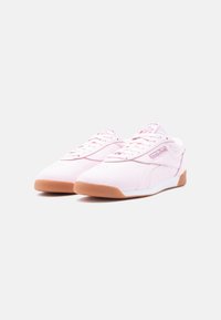 Ζευγάρι ανοιχτόροζ αθλητικά παπούτσια Reebok με καφέ σόλες, κορδόνια και ετικέτες με το λογότυπο, παρουσιάζονται σε λευκό φόντο.