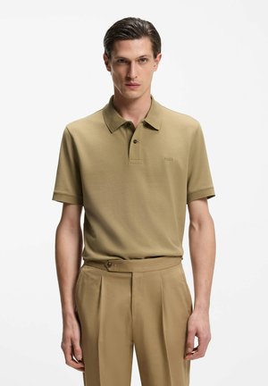 Polo de manga corta en verde oliva, con un cuello clásico y un pequeño logo bordado. Tejido suave y texturizado combinado con pantalones a medida.