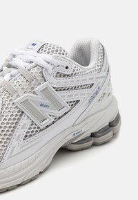 Baltas sporta kurpes ar sietu augšdaļu, sudraba akcentiem, mīkstu apkaklīti un pelēku zoli ar redzamu amortizācijas tehnoloģiju. Modelis "1906R."