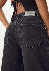 Črne denim hlače z sproščenim krojem, visokim pasom, dvema zadnjima žepoma in sivo oznako blagovne znamke na pasu.
