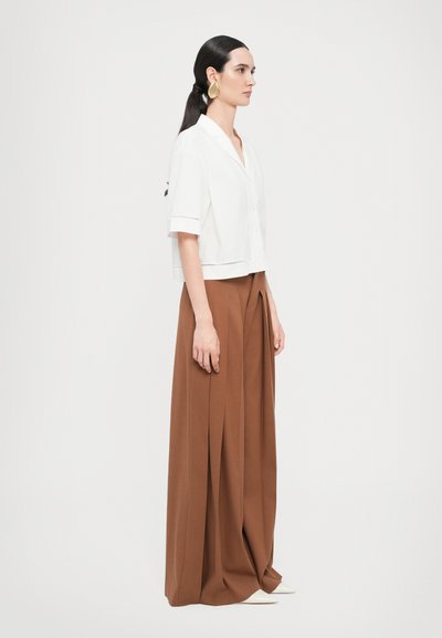 White cropped button-up shirt with short sleeves, paired with long brown pleated trousers. Smooth fabric with a simple design and cut.