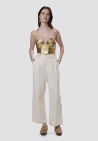 Top bustier metálico dorado con diseño acanalado, combinado con pantalones de pierna ancha crema de tiro alto y sandalias de plataforma marrones.