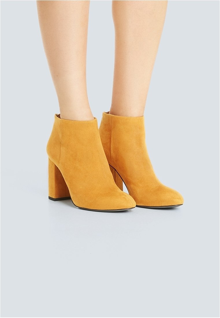 Bottes à cheville en daim jaune avec un bout arrondi et un talon épais. Texture lisse et détails minimaux. Construction robuste.