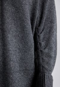 Pull en maille gris foncé avec une surface texturée, présentant des détails froncés sur les manches et des poignets côtelés. Matière douce et coupe près du corps.