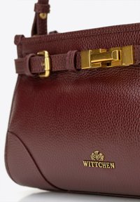 Bordeaux lederen handtas met een gestructureerde afwerking, voorzien van gouden hardware en een decoratief riemdetail met een sluiting. Merkennaam "WITTCHEN" in reliëf.