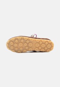 Semelle de chaussure avec une bande de roulement en caoutchouc beige présentant des grips circulaires de différentes tailles, attachée à une tige marron avec des lacets visibles.