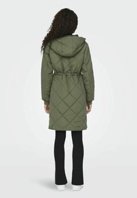 Olivgrüner, gesteppter Langmantel mit Kapuze, tailliertem Schnitt und langen Ärmeln. Verfügt über ein Rautenmuster und seitliche Taschen.