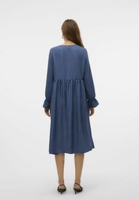 Modra obleka z dolgimi rokavi iz teksturiranega blaga, sproščenega kroja in z nabranim pasom. Dolžina do sredine Tele, okrogli izrez in diskretne balonske rokave.