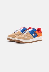 Zapatillas de deporte en tonos marrón y azul con acentos rojos, que presentan un upper de ante texturizado, cordones blancos y una suela de goma con surcos. Detalle del logo presente.