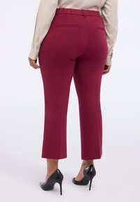 Pantalons bourgogne avec une texture lisse, dotés d'une taille haute, d'une coupe droite et de deux poches arrière, associés à des escarpins noirs.