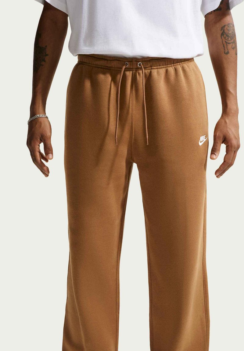 Pantalon de survêtement marron avec taille à cordon de serrage, en matériau doux. Présente un logo Nike blanc sur la cuisse gauche. Aucun motif visible.