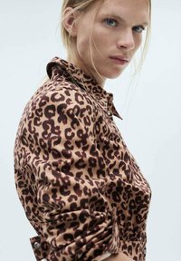 Hnedobéžová košeľa s leopardím vzorom, so golierom, detailmi na gombíky a zvinenými rukávmi. Hladká tkanina so štruktúrovaným strihom.