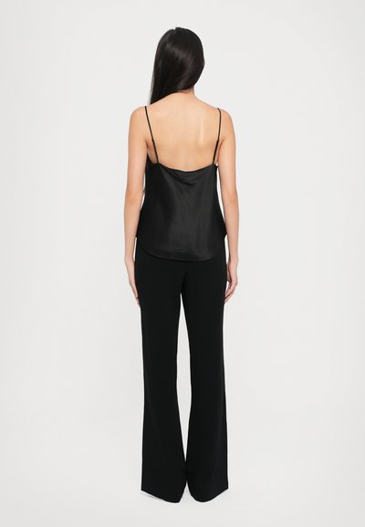 Musta satiininen camisole ohutolkaimilla, jossa on matala selkäosa, yhdistetty korkeavyötäröisiin mustiin housuihin, jotka ovat virtaviivaiset ja leveät lahkeet.
