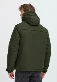 Giacca isolante di colore verde scuro con cappuccio, caratterizzata da una superficie liscia e polsini elastici. Design semplice senza loghi o dettagli visibili.