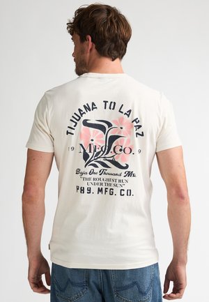 Kort mouwzijde, crème kleurig t-shirt met een zwart-roze afbeelding op de achterkant met bloemmotieven en tekstelementen.