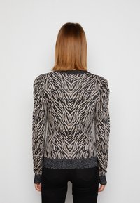 Maglione a strisce zebrate in beige e nero, in materiale lavorato a maglia con spalle strutturate, polsini e orlo a coste, caratterizzato da una leggera lucentezza.