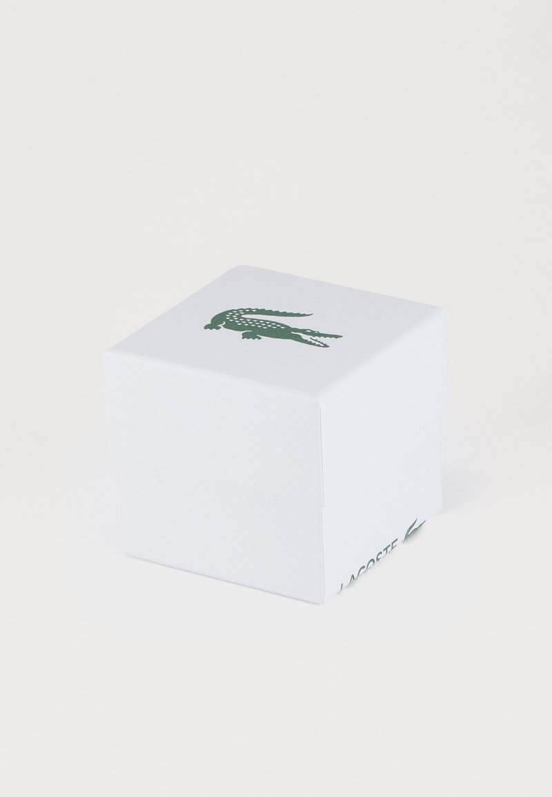Caja cuadrada blanca con un logo de cocodrilo verde en la tapa. Presenta un acabado texturizado y un diseño sin costuras, sin hardware visible.