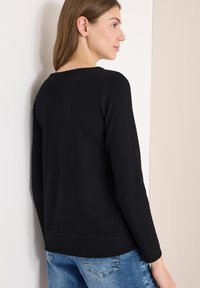 Maglia a maniche lunghe nera a coste con scollo ampio, caratterizzata da una vestibilità comoda e tessuto strutturato. Abbinata a jeans di denim azzurro chiaro.