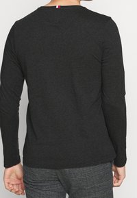 Langärmliges, rundhalsiges Shirt in Anthrazit. Hergestellt aus weichem Stoff, mit einem kleinen farbigen Akzent am Nacken hinten.