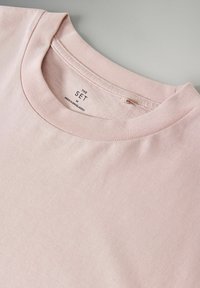 Hellrosa Baumwoll-T-Shirt mit Rundhalsausschnitt, kurzen Ärmeln und einem Etikett innen, das "THE SET" und Pflegeinformationen anzeigt.
