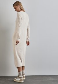 Abito lungo beige a coste con maniche lunghe, tessuto testurizzato, fessure laterali, abbinato a sneakers alte beige e bianche e calzini leggeri.
