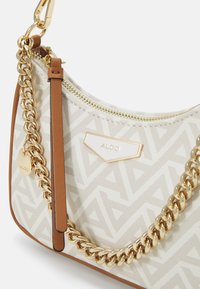 Sac à main blanc avec motif géométrique, chaîne en or et éléments en métal doré, accents en cuir marron, fermeture à glissière et détail de logo à l'avant.