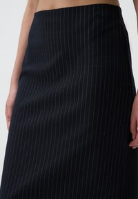 Jupe crayon bleu marine avec des rayures verticales. Fabriquée en tissu texturé, dotée d'une taille ajustée et d'une silhouette droite.