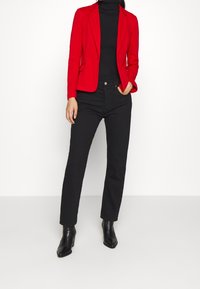 Red fitted blazer, black high-neck top, black straight-leg jeans, and black heeled ankle boots. Smooth fabric with tailored accents.