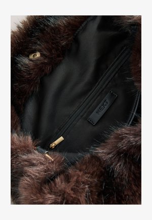 Binnenkant van een bruine imitatiebonttas met een zwarte voering, een zakje met ritssluiting en een klein zwart label met "NEXT." Zichtbare gouden ritssluiting hardware.