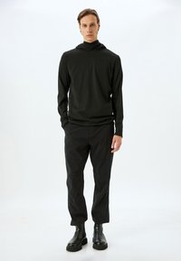 Sort langærmet hættebluse parret med sorte tapered bukser og sorte ankelstøvler. Stoffet fremstår glat med en tætsiddende pasform.