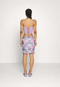 Top lilás com costas amarradas em rendas, combinado com uma saia lápis de padrão multicolorido. Footwear apresenta saltos bloco chunky lilás.