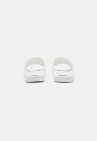 Sandale albe tip slide cu un finisaj neted, cu spatele deschis și talpă flată. Design minimalist fără modele sau accente suplimentare.