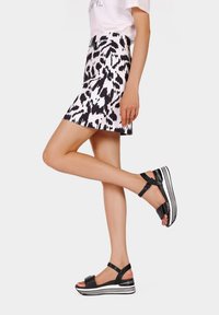 Sandali platform neri con una finitura texturizzata, dotati di una larga cinghia alla caviglia e suola a righe bianche. Indossati con una gonna a fantasia contrastante.