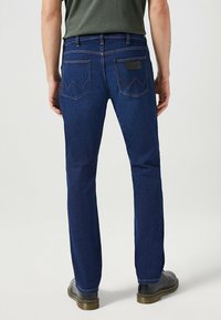 Vaqueros oscuros de hombre en azul marino con corte ajustado, que cuentan con dos bolsillos traseros y costuras en contraste. Fabricados en tela de mezclilla, de textura suave.