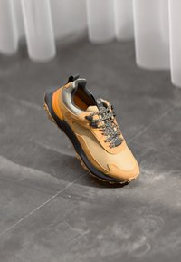 Żółte i szare buty sportowe z teksturowaną cholewką, wzmocnionym czubkiem, wytrzymałą podeszwą i czarnymi akcentami. Posiadają system szybkiego sznurowania.