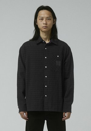 Black checkered shirt made from soft fabric, featuring a button-down collar, front pocket, and white buttons. Structured, relaxed fit.