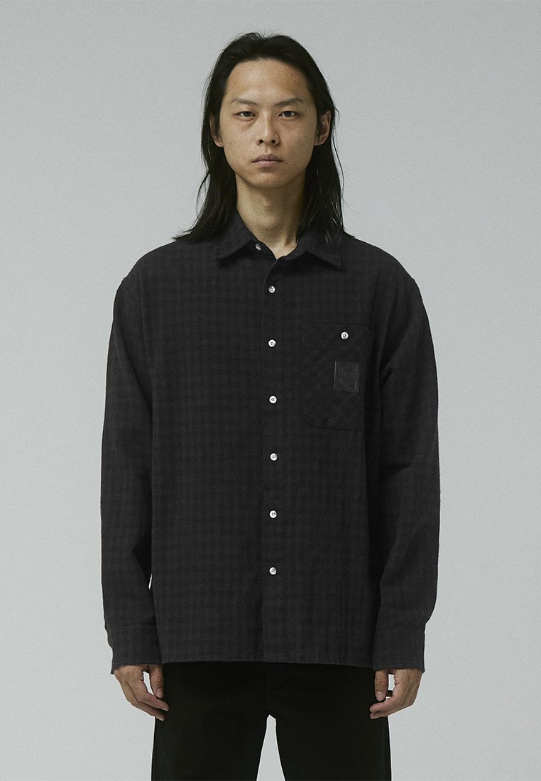 Black checkered shirt made from soft fabric, featuring a button-down collar, front pocket, and white buttons. Structured, relaxed fit.