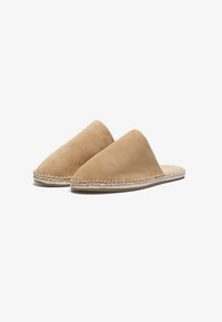 Beige semsket slip-on sko med spiss tå og flettet jute såle. Glatt tekstur med minimalistisk design og ingen synlige lukkemekanismer.