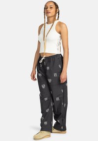 Hvid ribbet crop top og sorte drawstring bukser med hvide dyremærker. Bukserne har en løs pasform og lommer. Beige fodtøj fuldender looket.